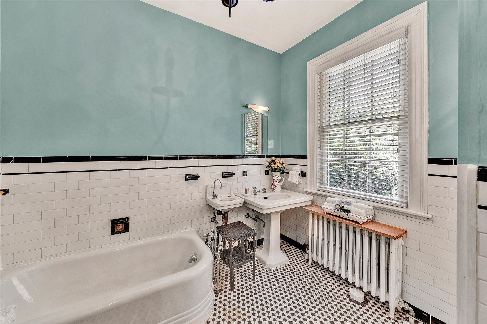Bright bathroom with mint walls, white tile, clawfoot tub, pedestal sink, and window blinds