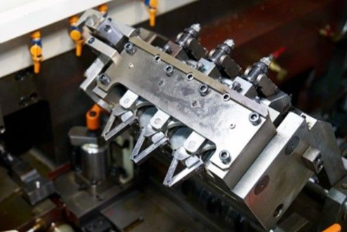 Close-up of a metallic industrial machine with various arms and nozzles; likely for manufacturing.