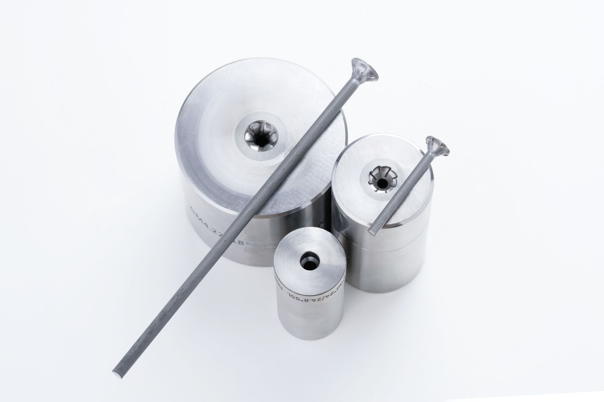 Three metal dies and two long, thin rods, on a white surface.