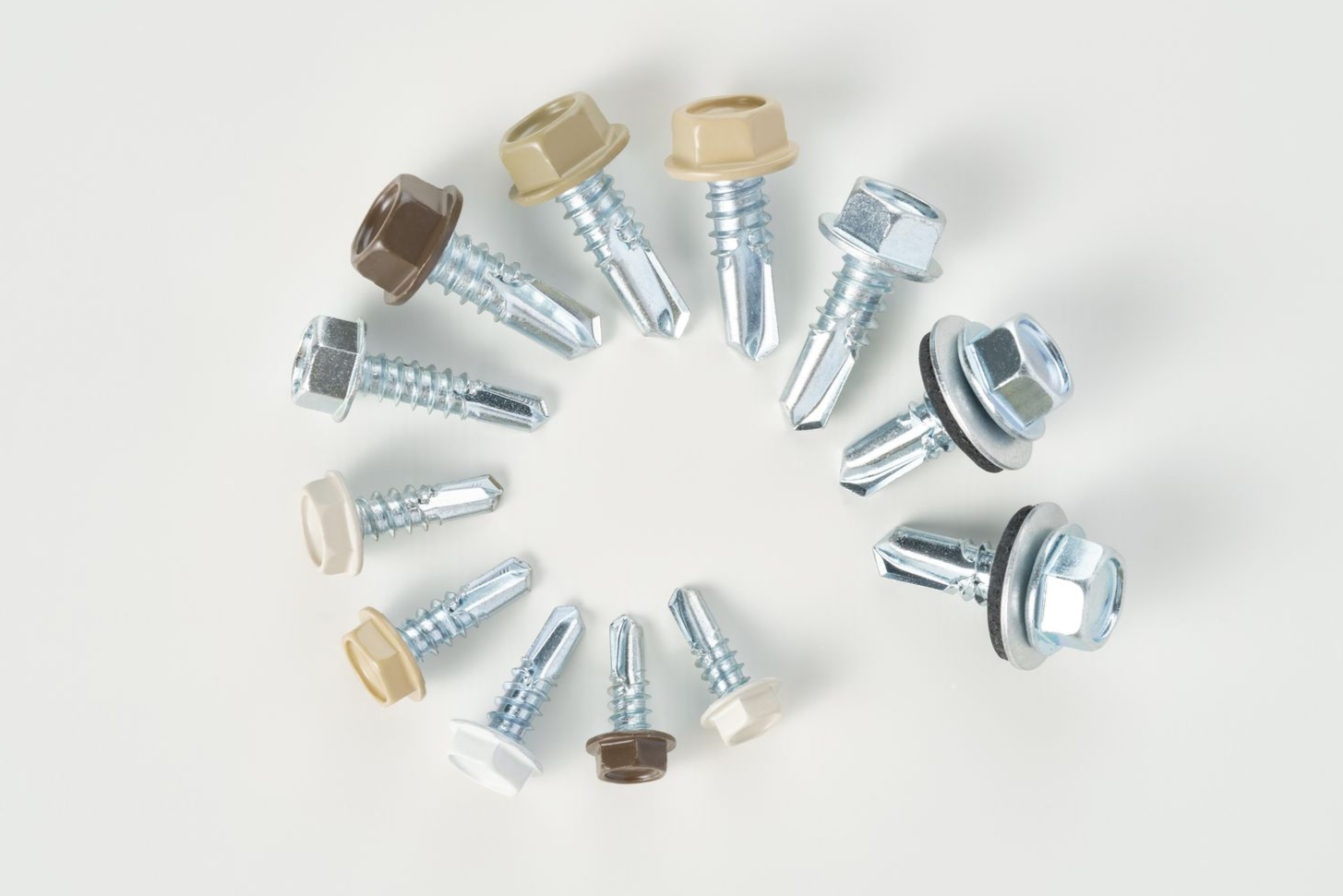 A circular arrangement of various colored metal screws with hex heads on a white surface.
