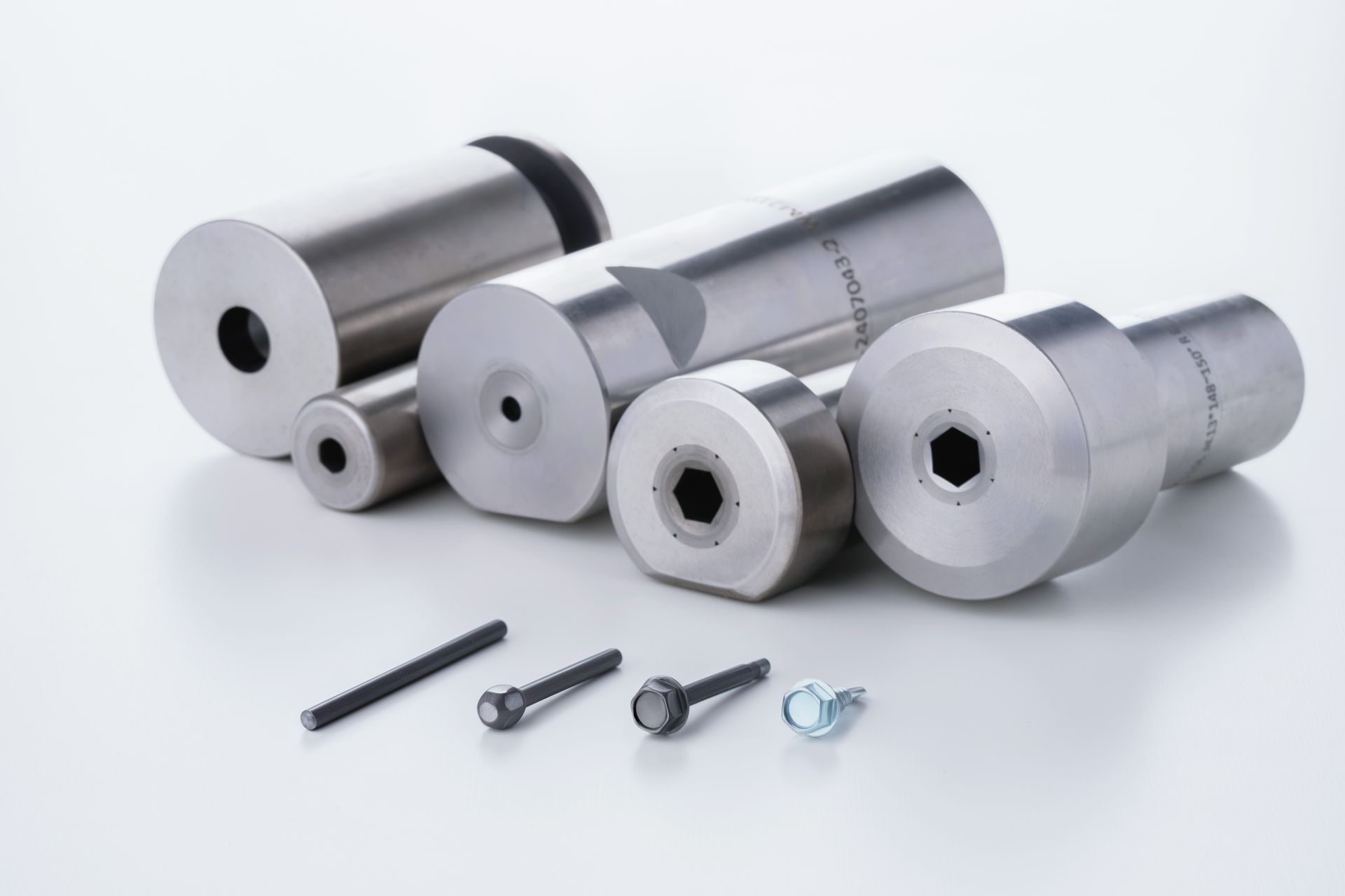 Metal extrusion dies and finished screws arranged on a white surface.