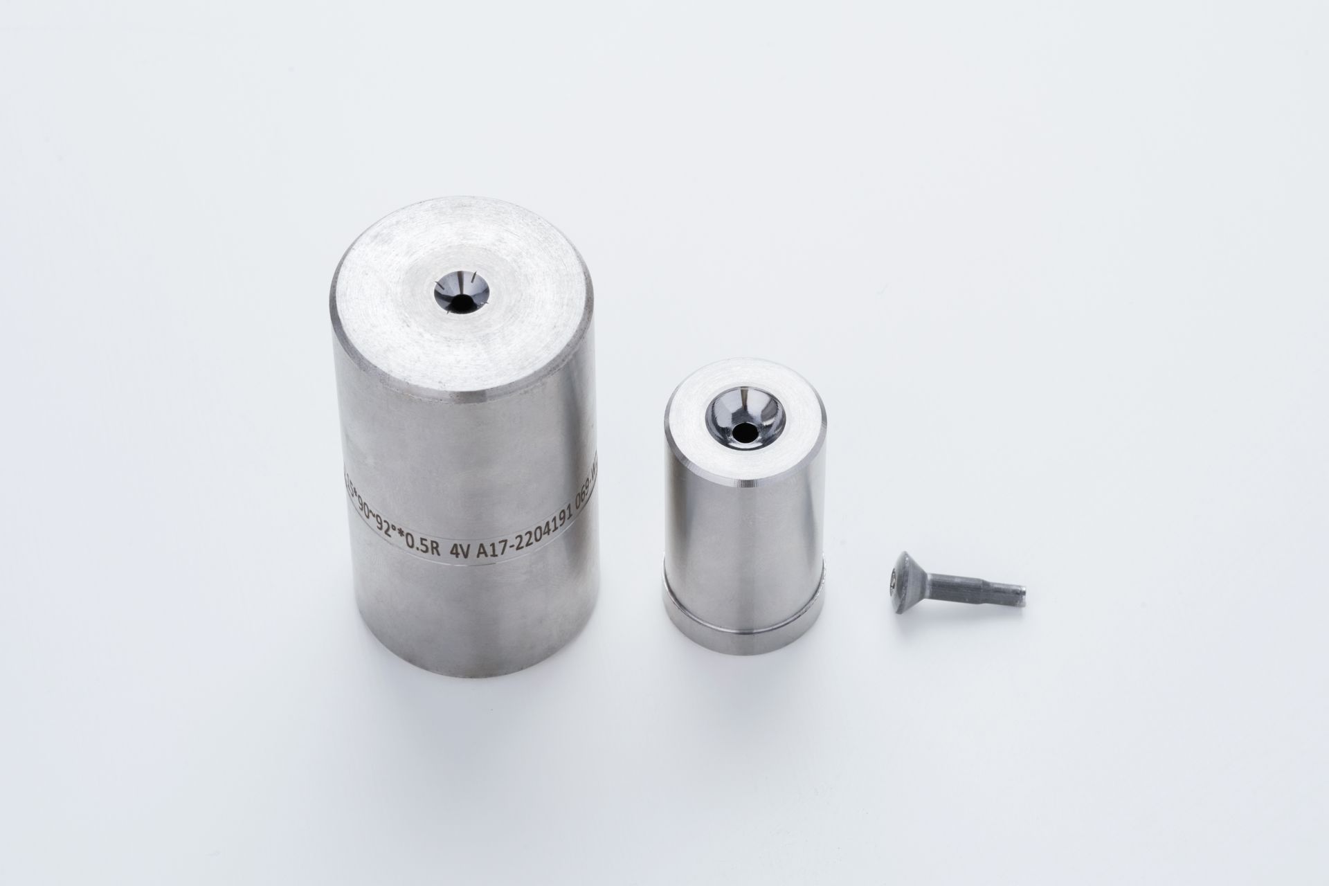 Metal die components and a screw, arranged on a white surface.