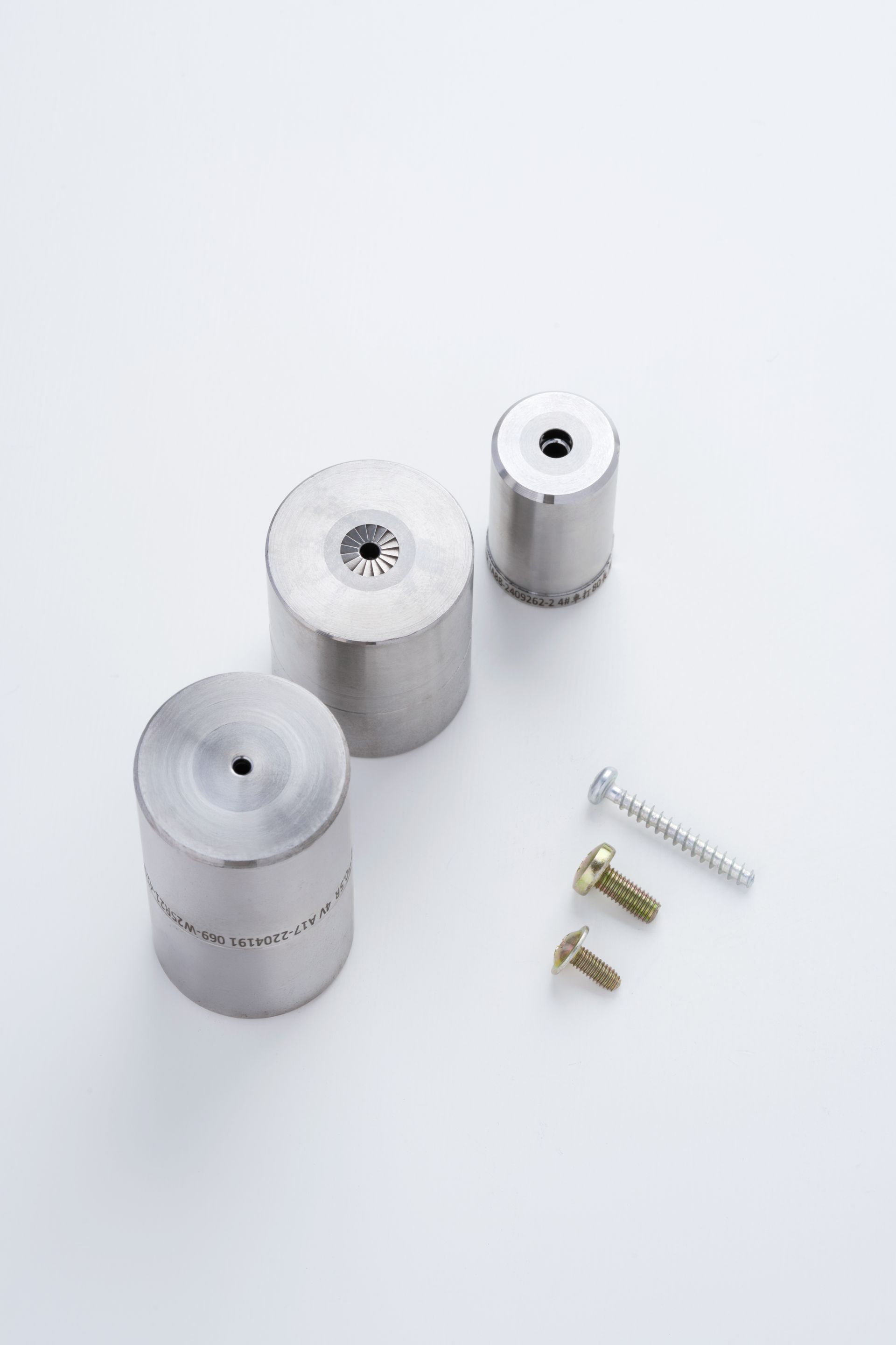 Three silver cylindrical metal dies and three screws on a white surface.