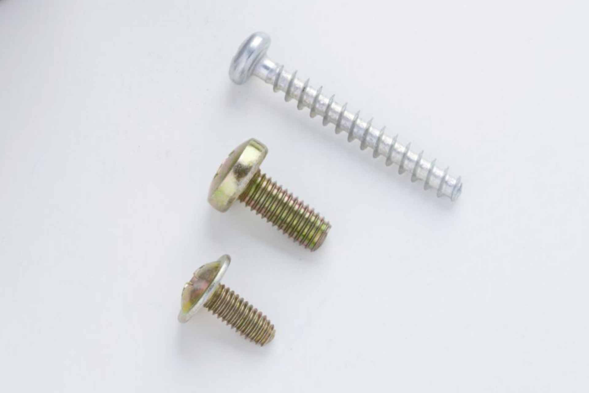 Three metal screws of varying sizes on a white surface.