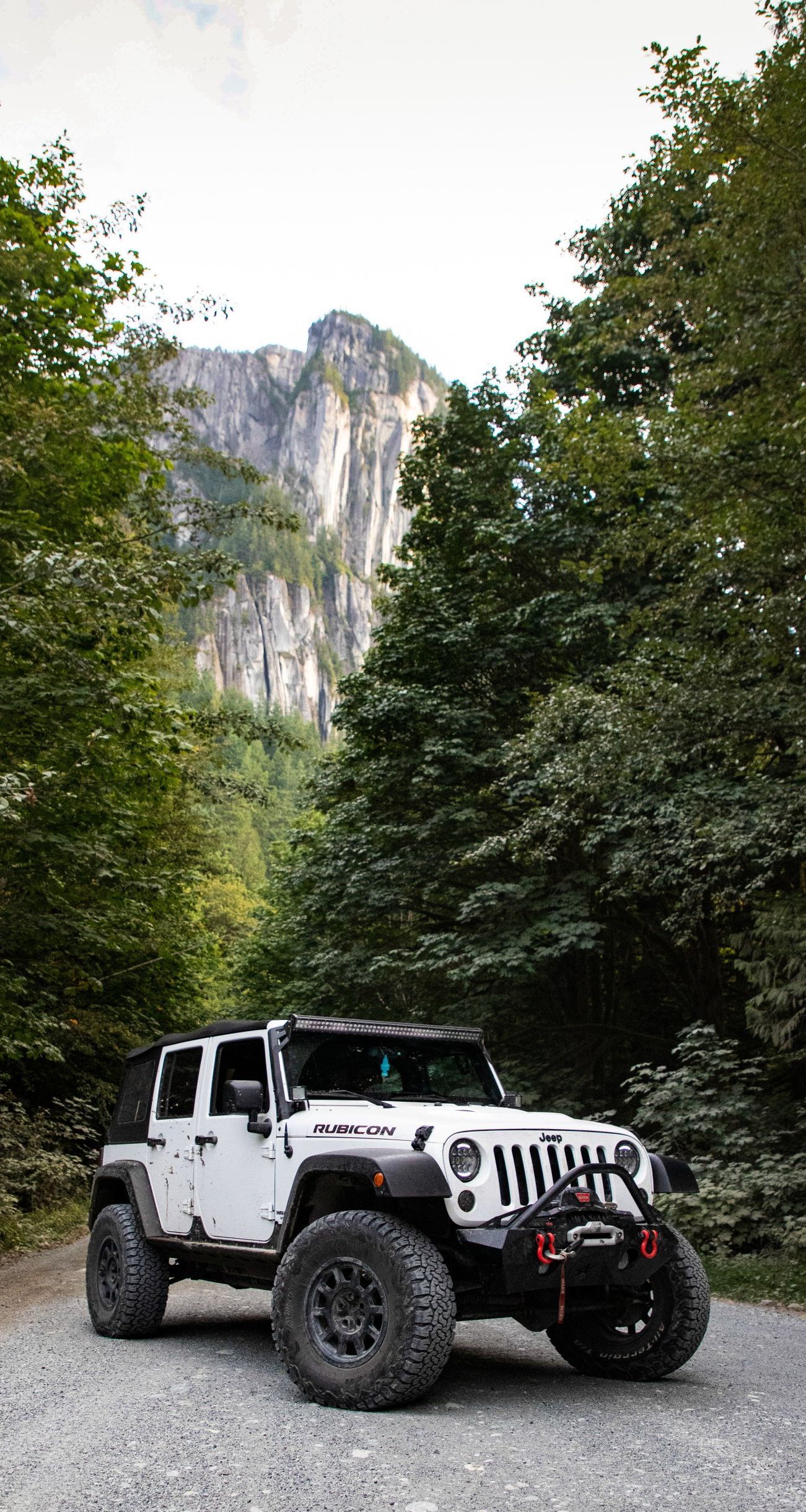 A white jeep is parked on a gravel road in front of a mountain.