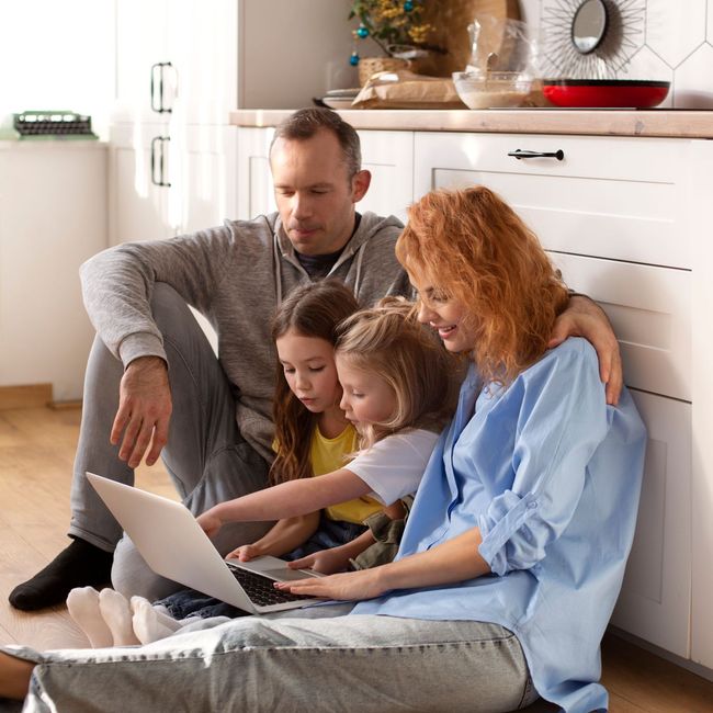 a family sits on the floor looking at a laptop