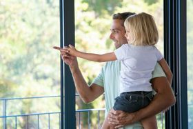 a man holds a little girl in his arms while they look out a window