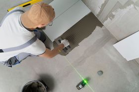 a man laying tiles on a floor with a green laser behind him