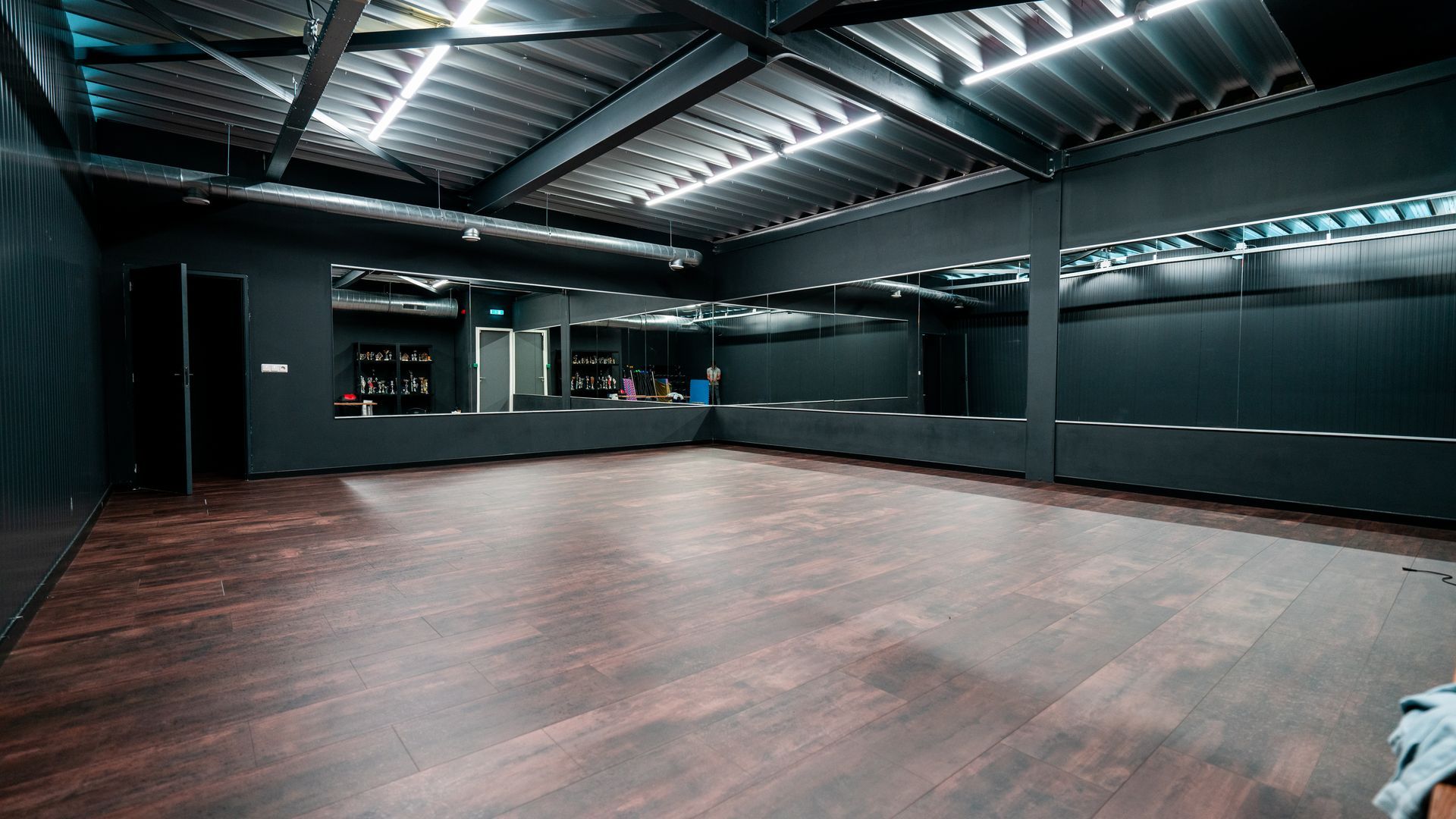 Een lege dansstudio met een houten vloer en spiegels.