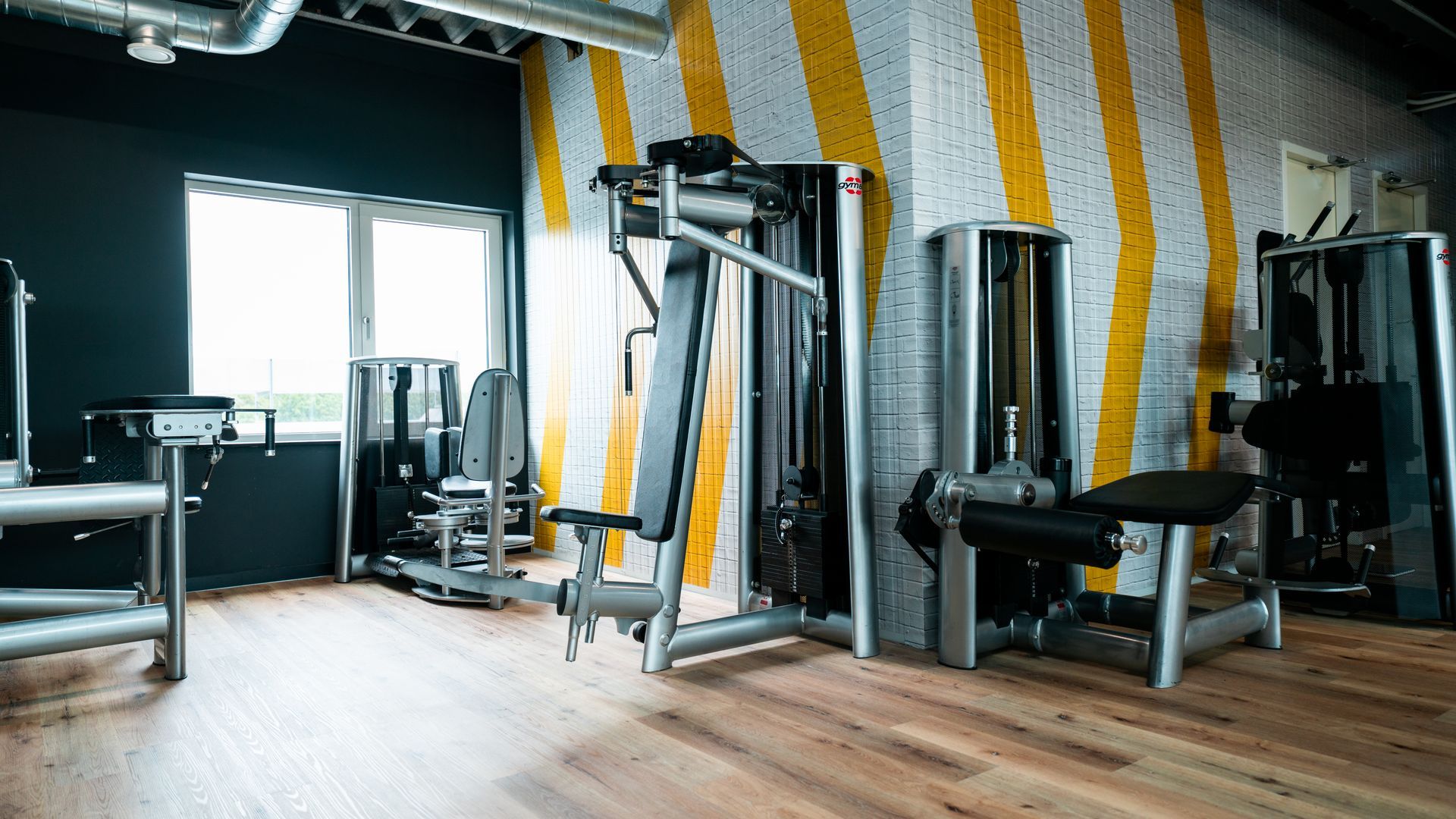 Een fitnessruimte met veel fitnessapparatuur en een houten vloer.