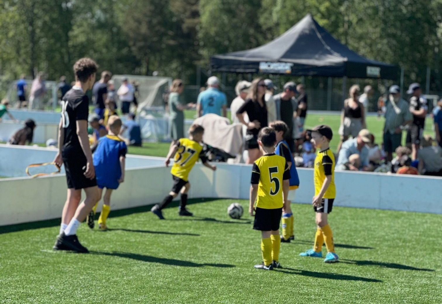 Barn som spelar fotboll på liten plan med sarg.