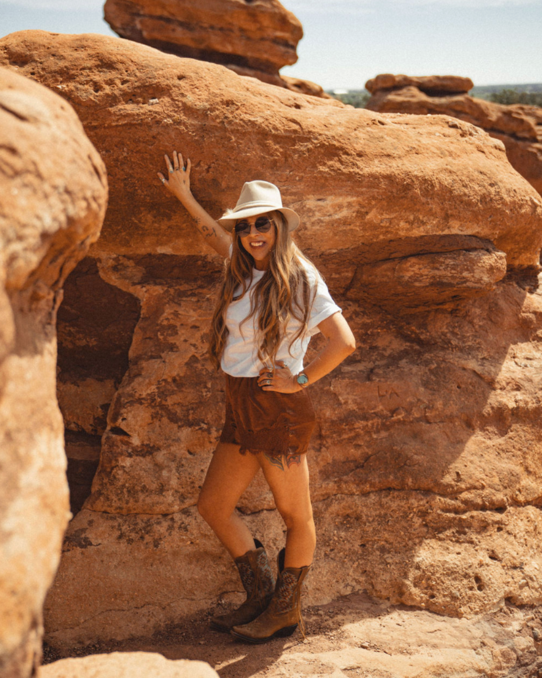 a woman wearing a hat and sunglasses stands in front of a wall