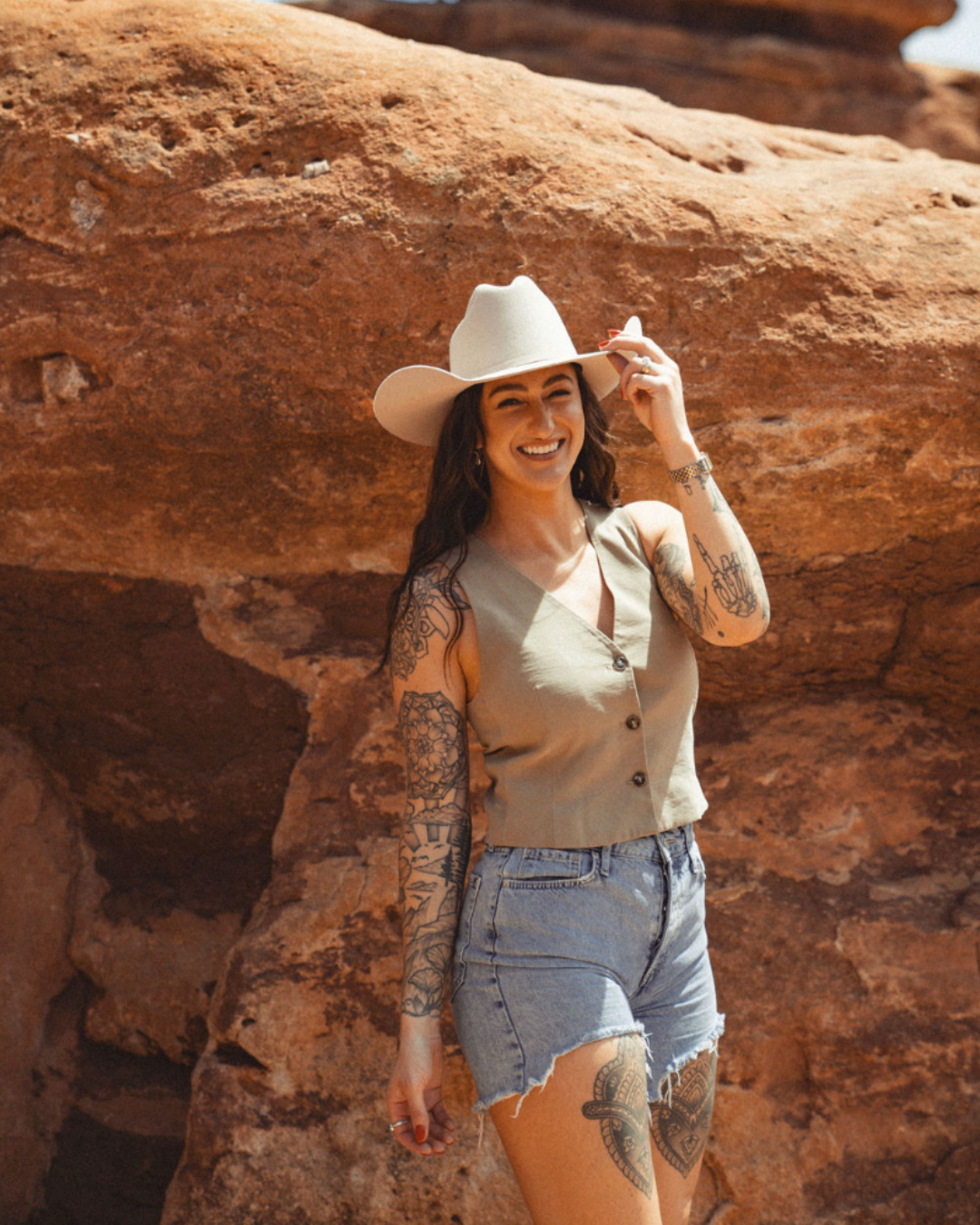 a woman wearing a hat and sunglasses stands in front of a wall