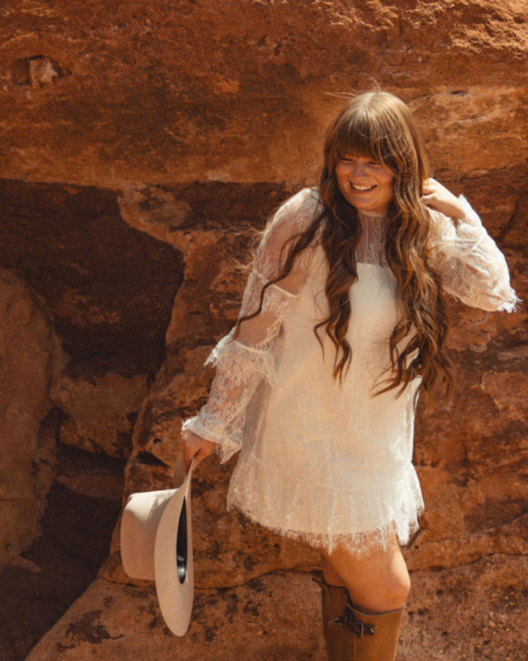 a woman wearing a hat and sunglasses stands in front of a wall