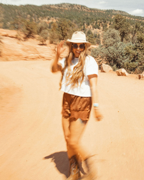 a woman wearing a hat and sunglasses stands in front of a wall