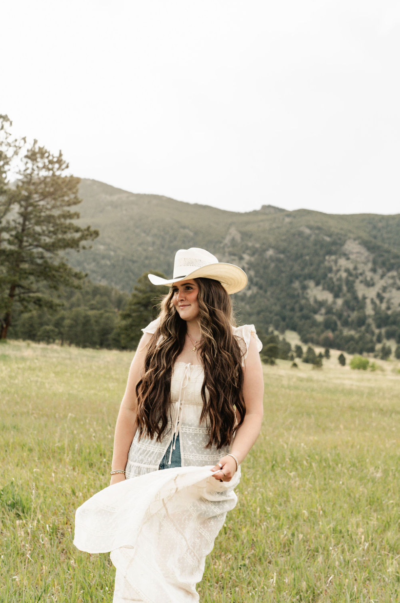 a woman wearing a hat and sunglasses stands in front of a wall