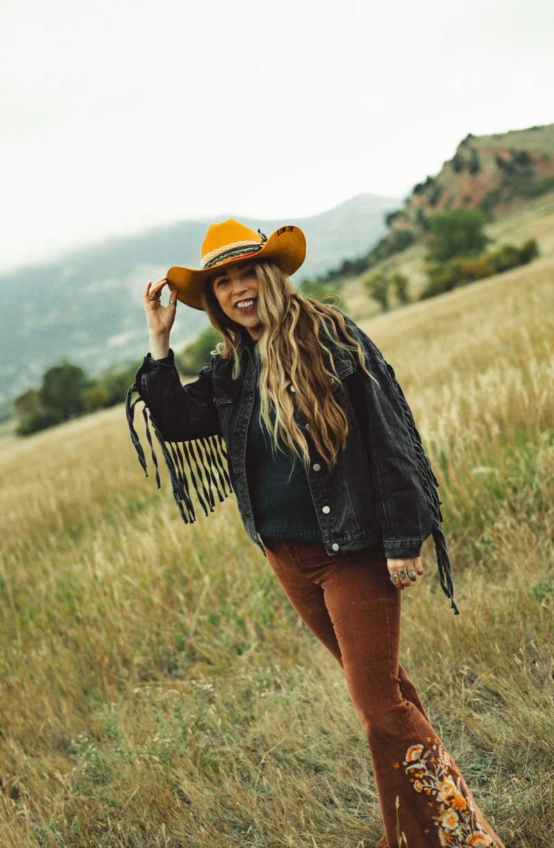 a woman wearing a hat and sunglasses stands in front of a wall