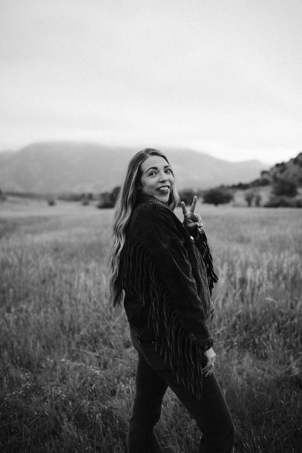 a woman wearing a hat and sunglasses stands in front of a wall