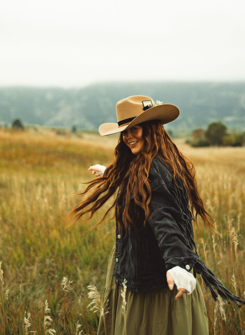 a woman wearing a hat and sunglasses stands in front of a wall