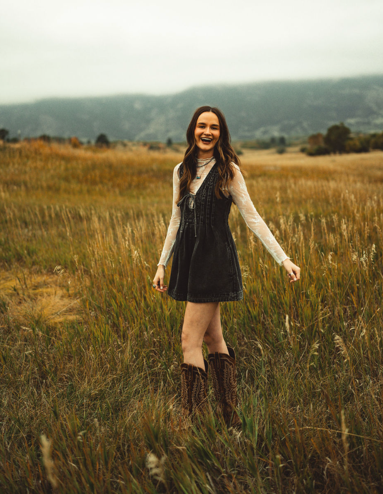 a woman wearing a hat and sunglasses stands in front of a wall