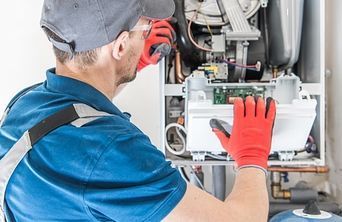 A man wearing red gloves is working on a boiler.