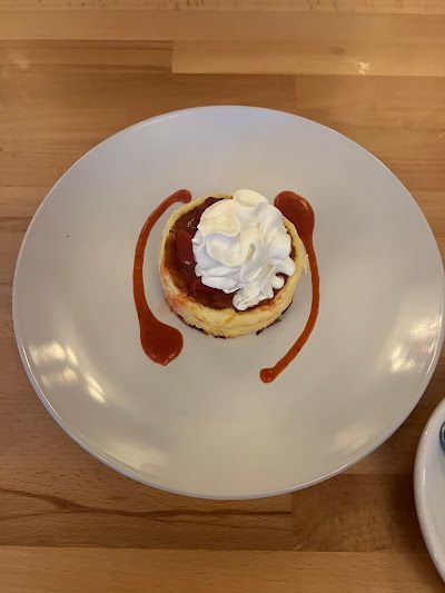 A white plate topped with a cheesecake with whipped cream and strawberry sauce