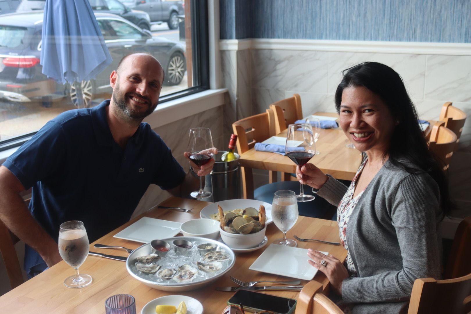 A man and a woman are sitting at a table inside of Drift Seafood restaurant holding wine glasses