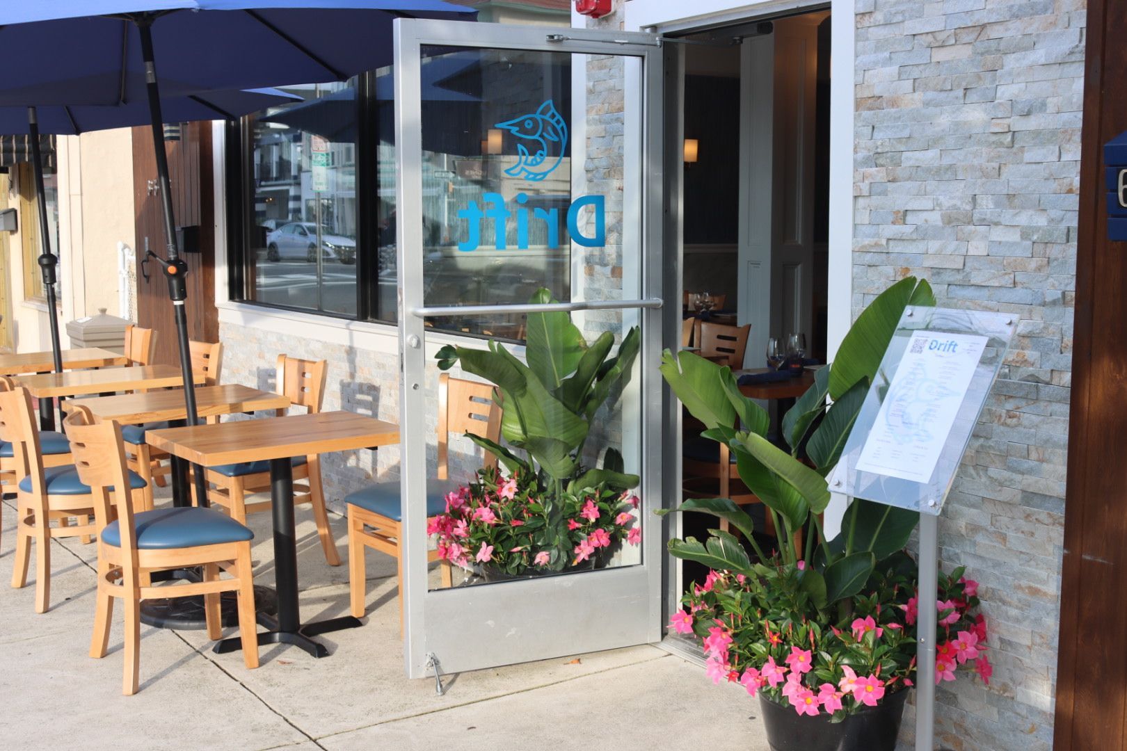 Entrance to Drift Seafood restaurant with outside tables, chairs, and umbrellas