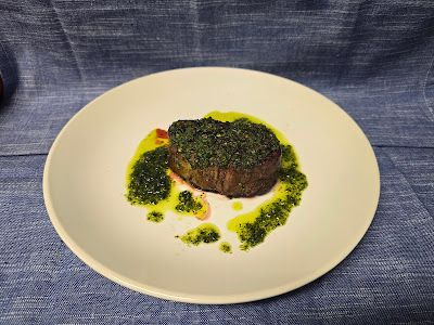 A white plate topped with a piece of filet mignon in chimichurri sauce