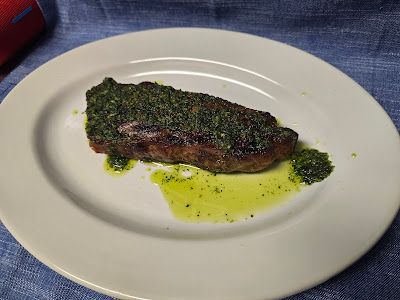 A white plate topped with a ny strip steak in chimichurri sauce