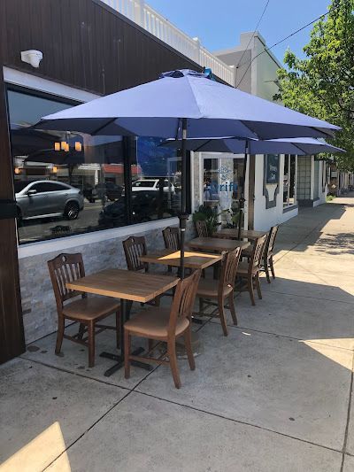 A patio with tables and chairs and umbrellas in front of drift seafood in ventnor city, nj