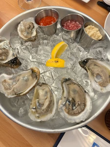 A tray of oysters on ice with sauces and a lemon slice