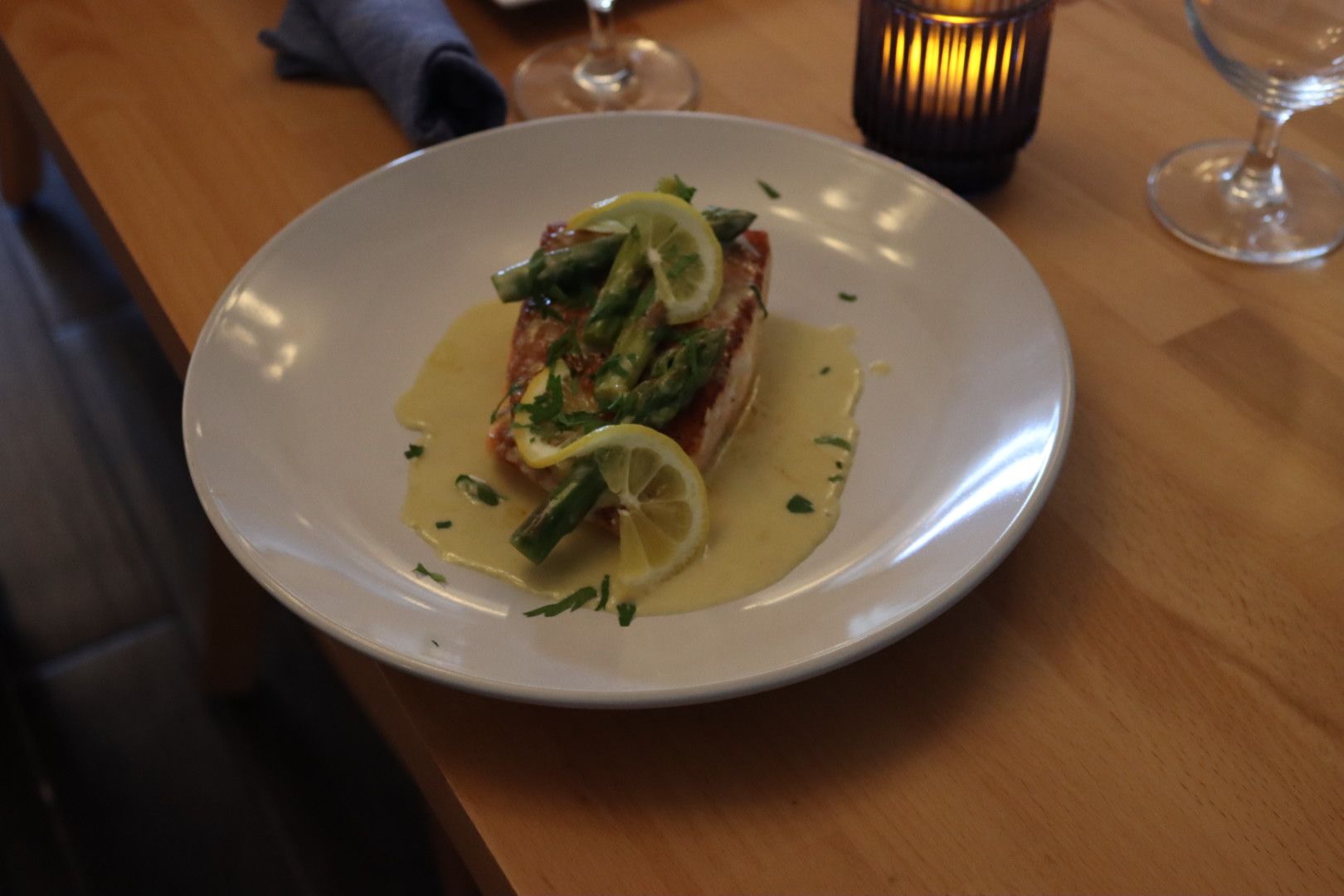 A white plate topped with a piece of pan seared salmon and asparagus on a wooden table