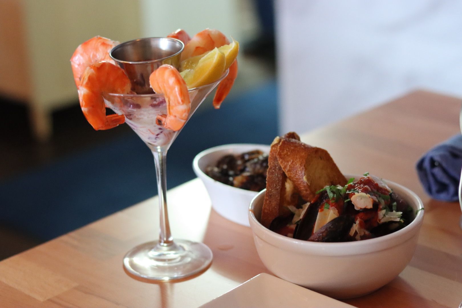 A martini glass filled with shrimp and a bowl of mussels marinara on a table