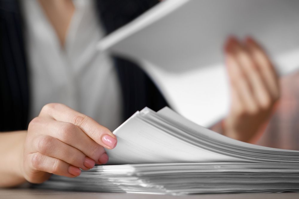 Woman's hands flipping through a stack of white papers, possibly documents, on a table — Immigration Agents in Cairns North, QLD