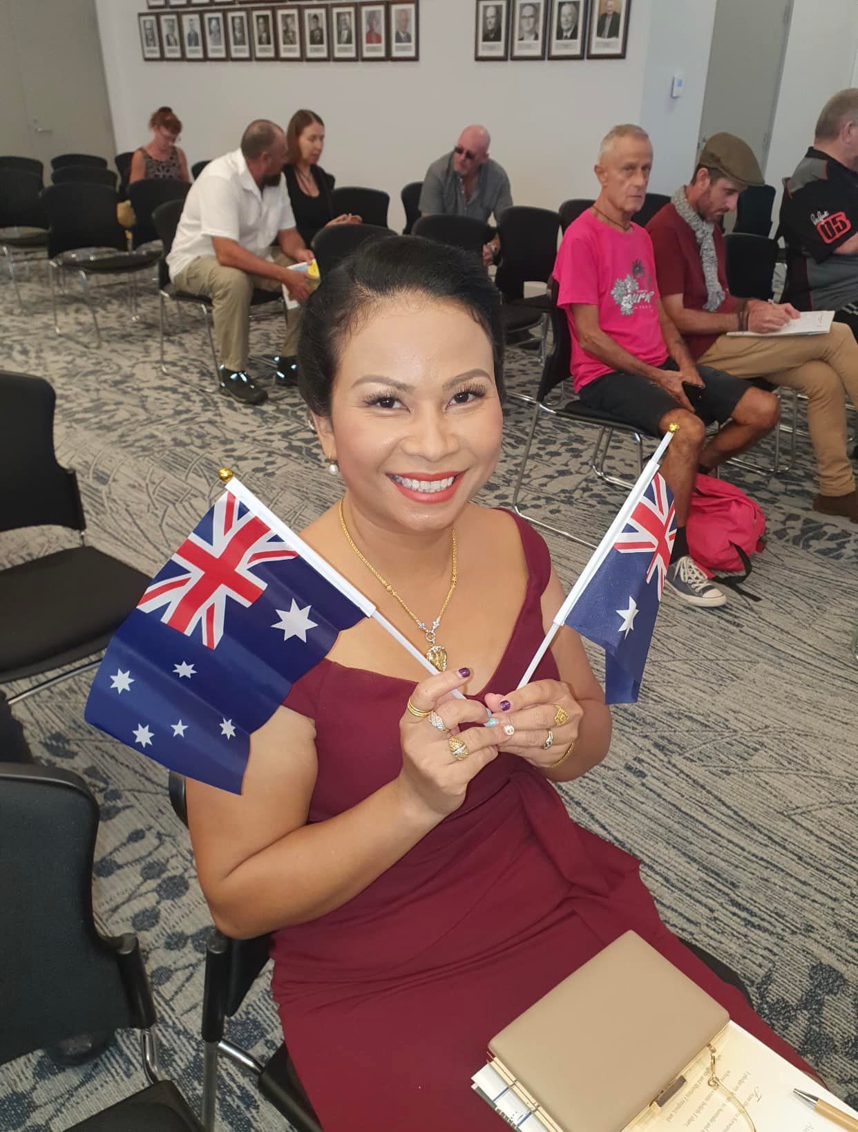 Woman in Burgundy Dress Smiles, Holding Two Australian Flags — Immigration Agents in Cairns North, QLD