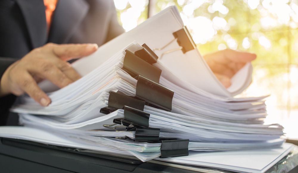 Person in suit, hands on a large stack of papers held together with clips, near a window — Immigration Agents in Cairns North, QLD