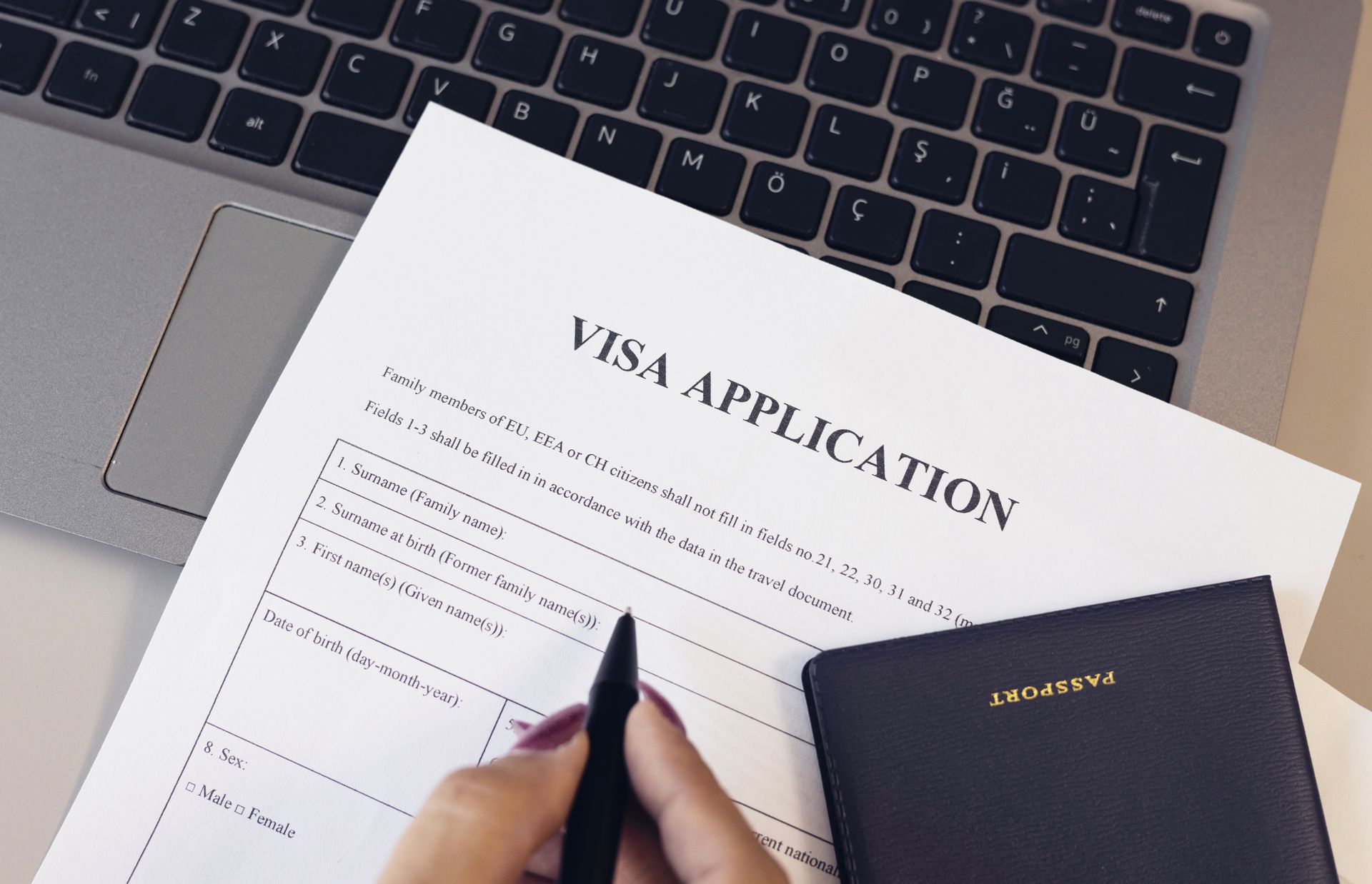 Hand Filling Out Visa Application Form With Laptop and Notebook on Desk — Immigration Agents in Cairns North, QLD