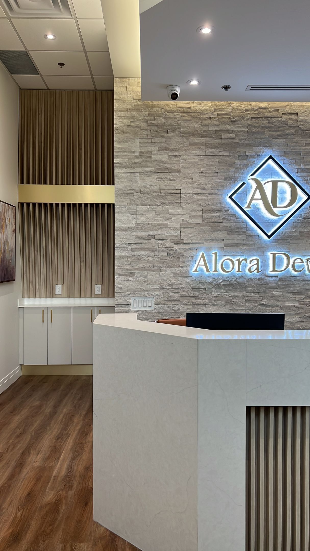 Reception area with white counter, textured stone wall, and illuminated logo