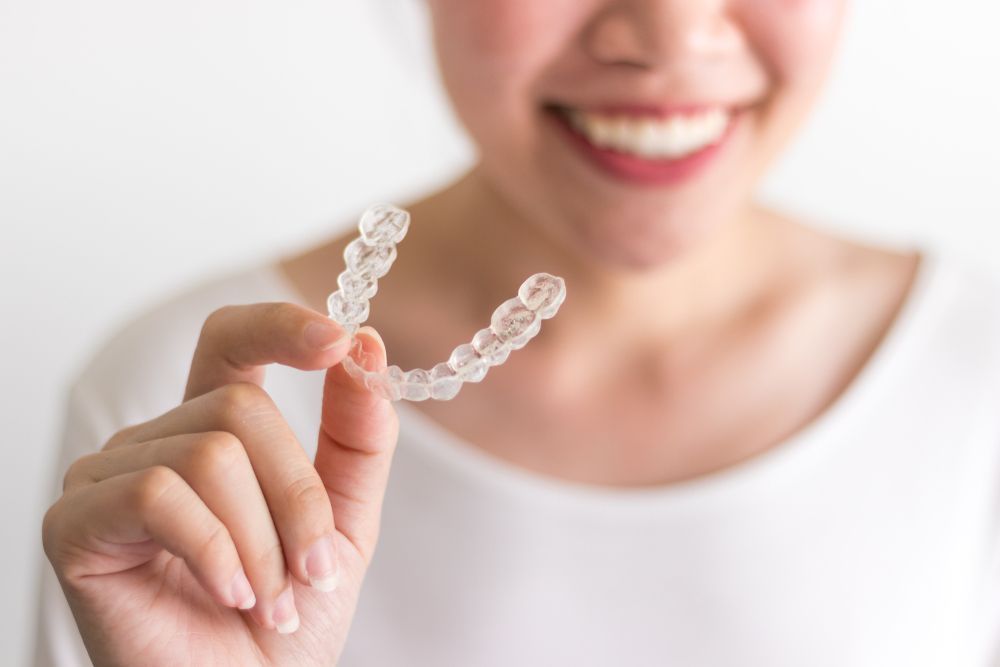 Person holding clear dental aligners and smiling in a white shirt