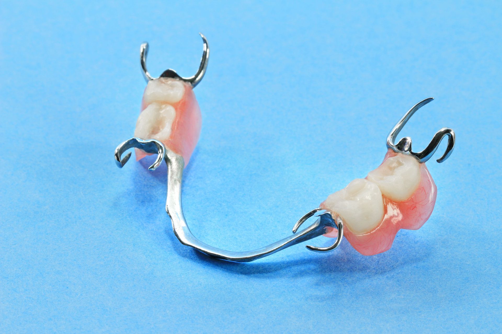 A partial denture with two pink artificial teeth and metal clasps on a blue background