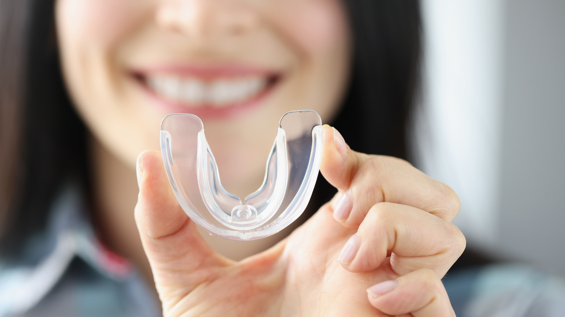 Woman holding a clear mouth guard, smiling with teeth visible.