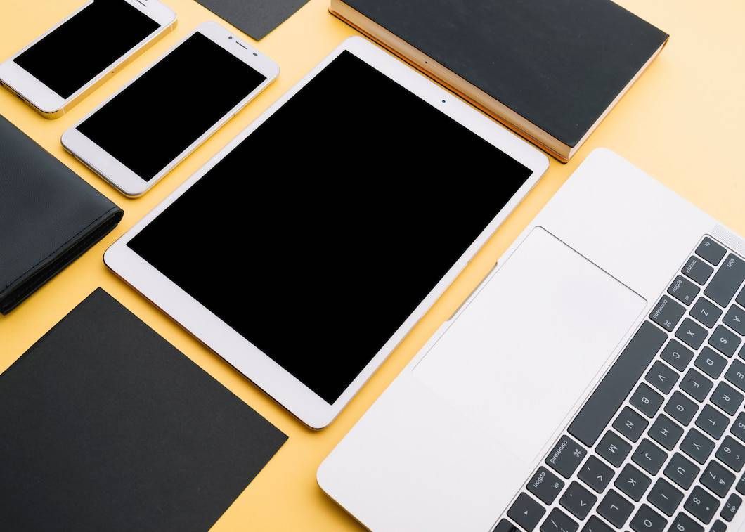 White tablet, phones, laptop, and black books on a yellow background.