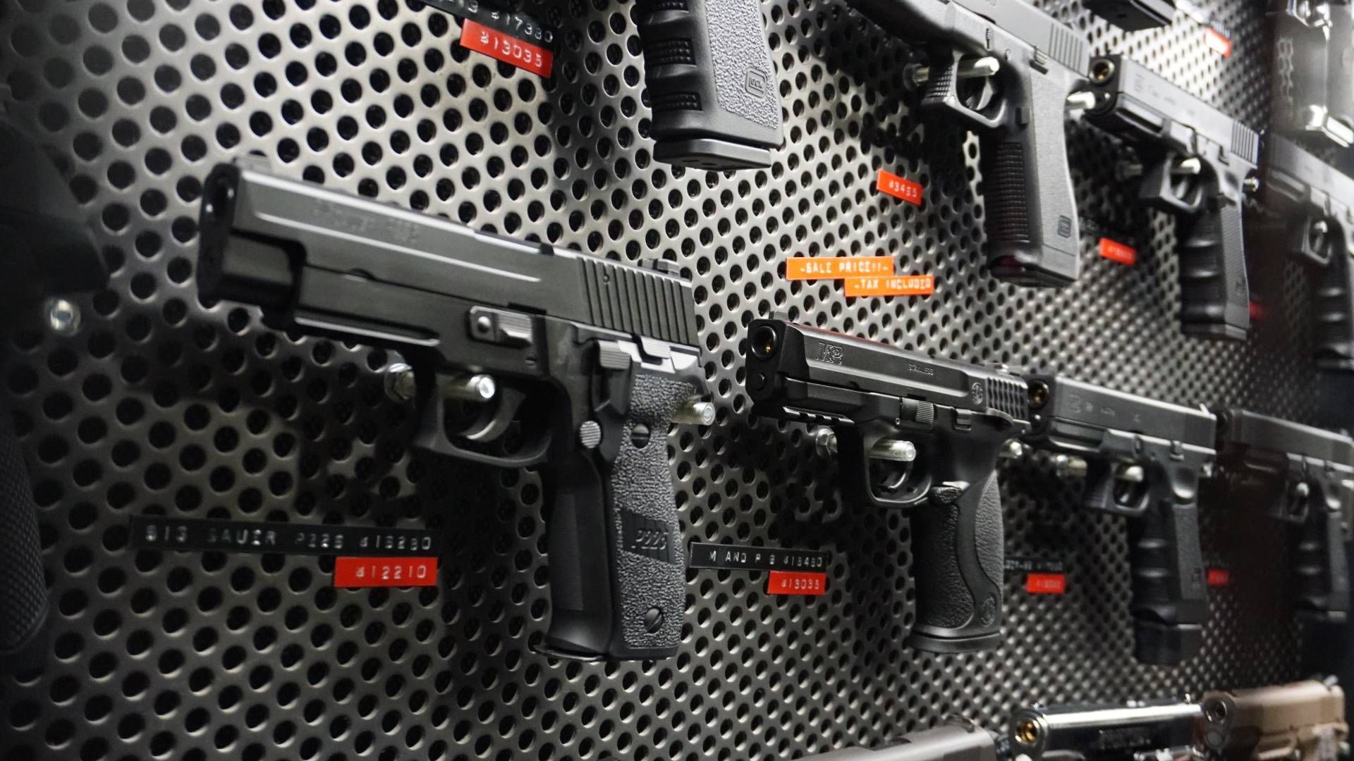 Guns displayed on a metal wall in a store. Black handguns are secured on the wall.
