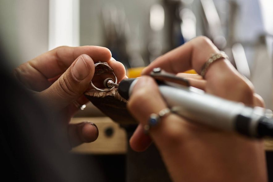 Jeweler using a tool to shape a ring, hands in focus, workshop setting.