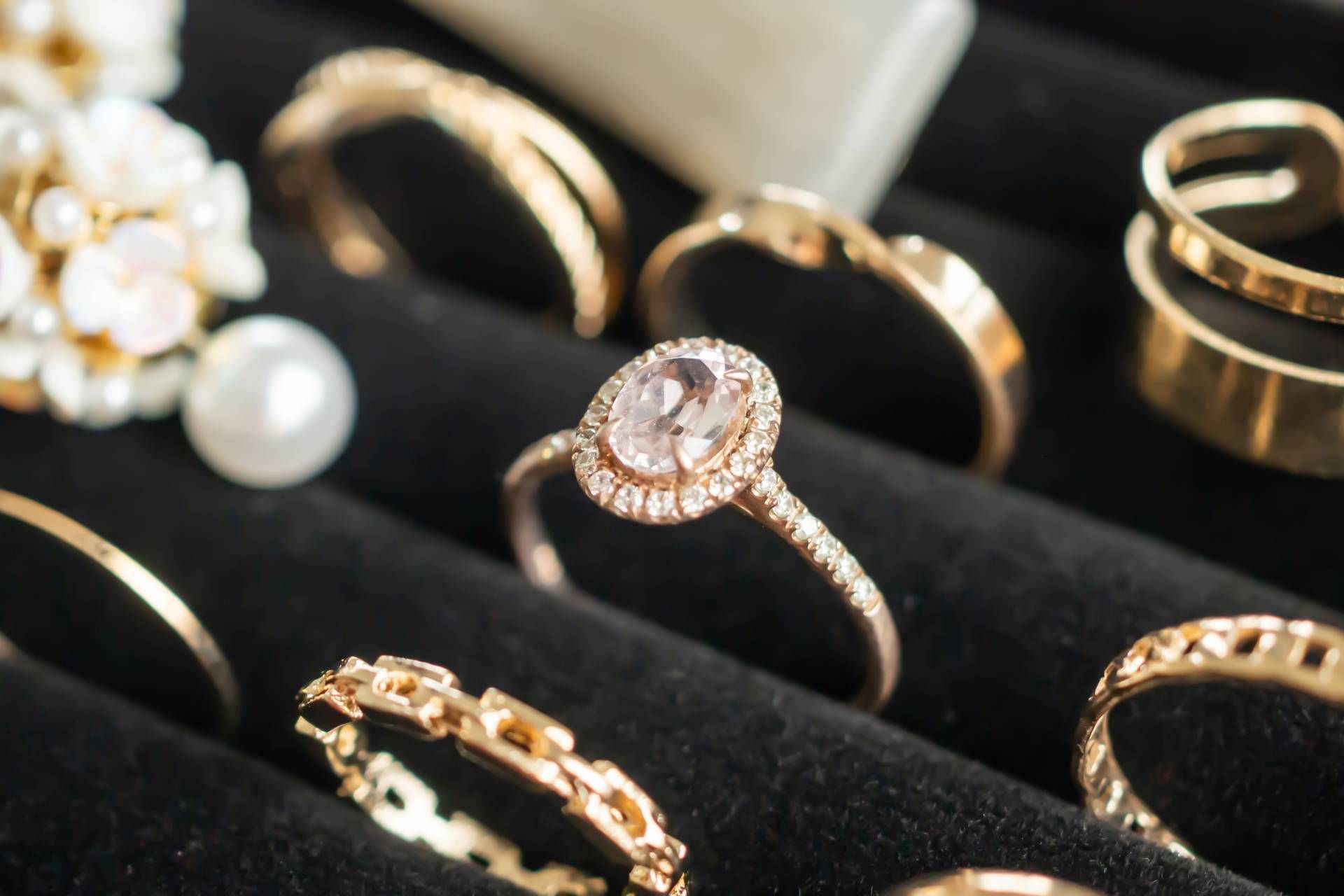 Jewelry display featuring gold rings with diamonds, pearls, and a black velvet background.