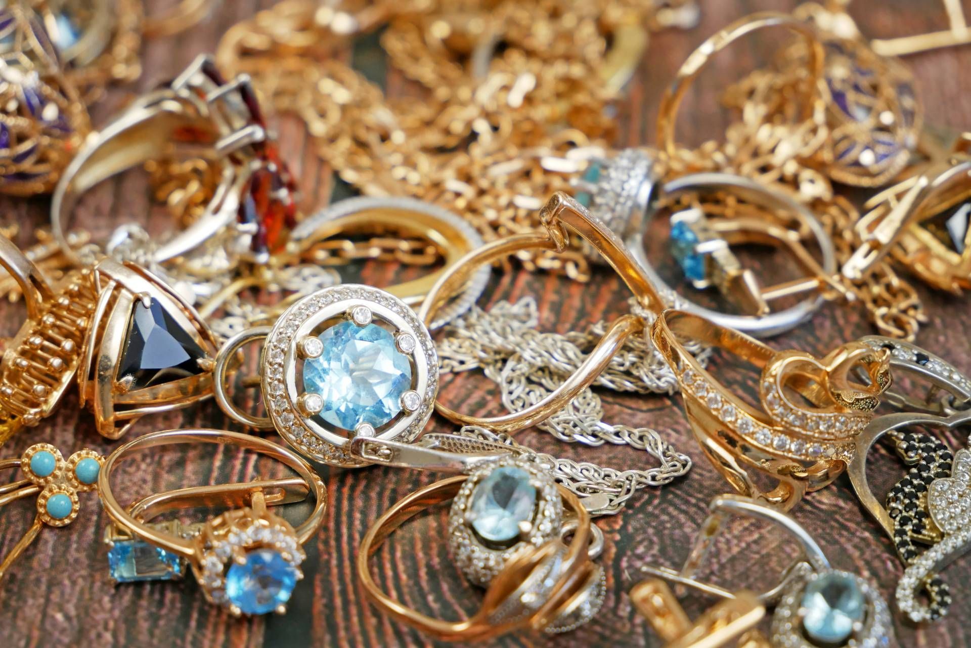Close-up of assorted gold and silver jewelry: rings, necklaces, and earrings with gemstones on wood.