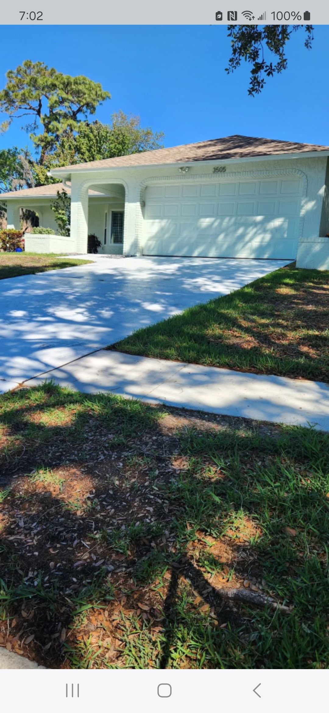 A white house with a concrete driveway and a lush green lawn.