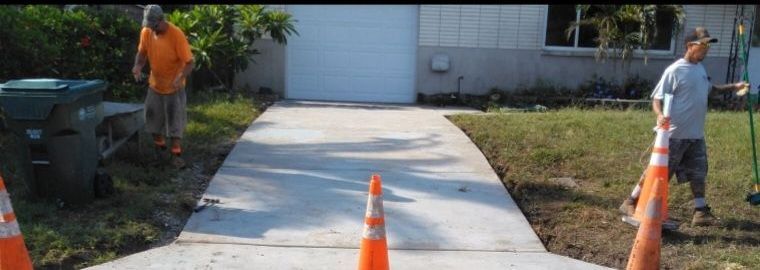 Two men are working on a concrete driveway in front of a house.