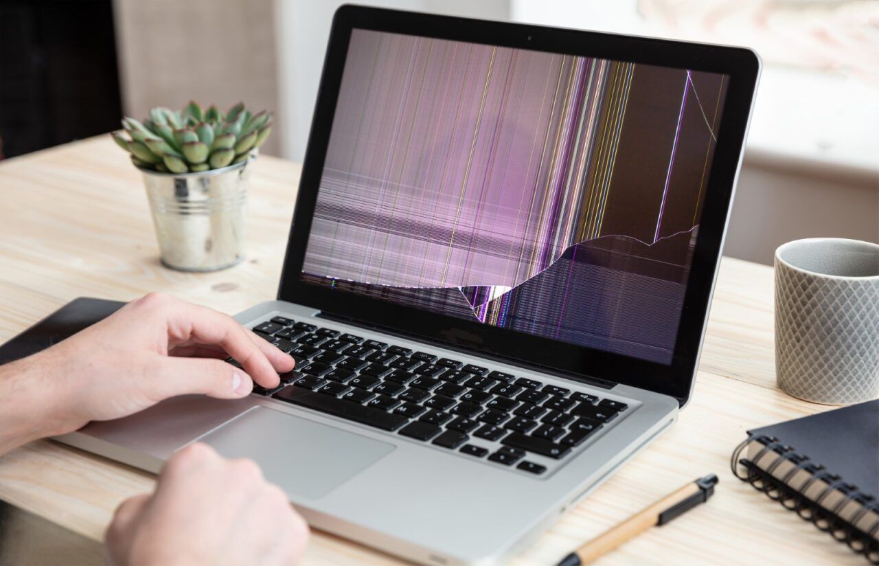 Person Using Laptop With Cracked Screen on Wooden Desk — Micromac Computers in Charmhaven, NSW